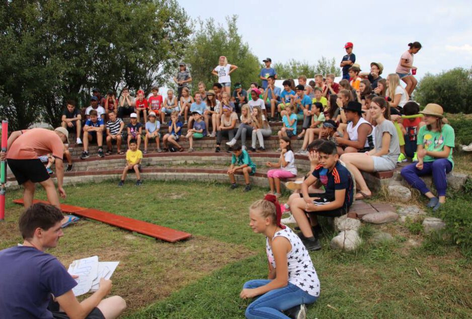 Chiemsee-Camp-Bild-4-1 ca 20 Kinder sitzen auf Stufen im Halbkreis und schauen bei einem Spiel zu