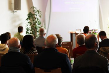 Gottesdienstraum von hinten mit 12 Persnen die nach vorne zum Pult schauen