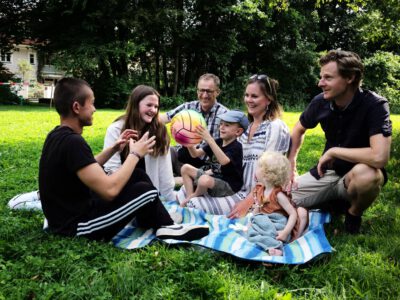L1008460 sieben Personen verschiedenen Alters sitzen auf einer Decke im Gras