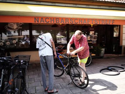 zwei Männer reparieren ein Fahrrad vor dem Laiimer Herz,