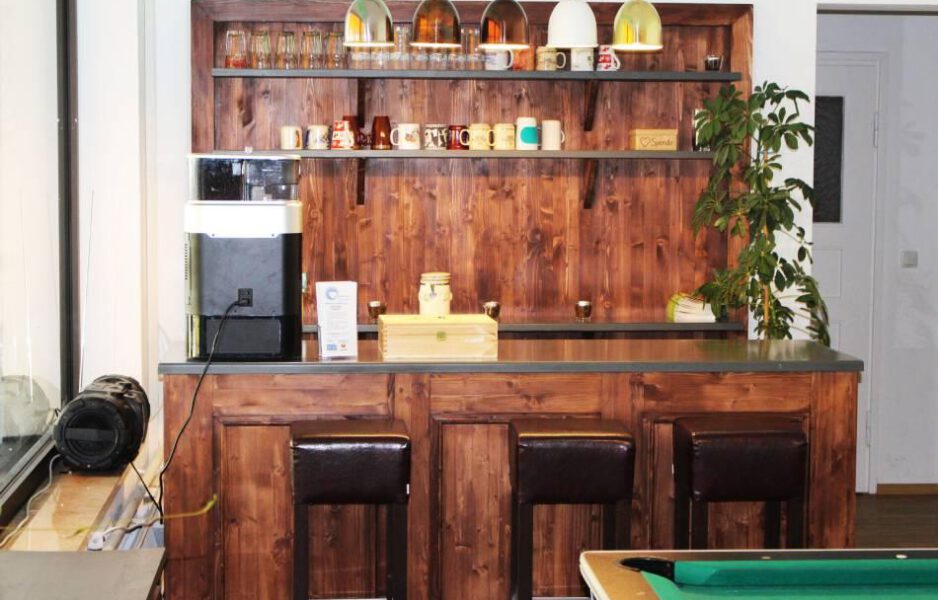 Laimer-Herz_innen_bearbeitet-scaled Innenansicht Nachbarschaftstreff Laimer Herz mit Holztheke und drei Leder-Stehhocker